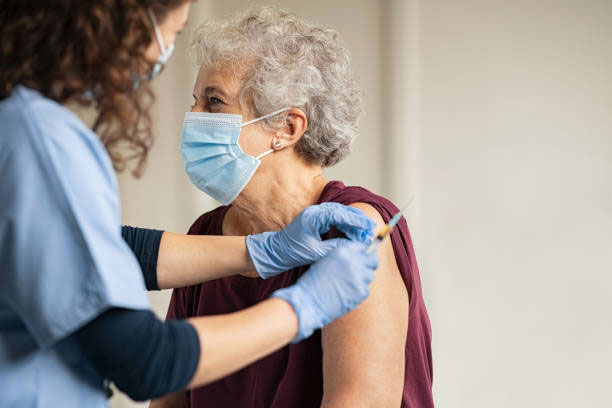 Elderly woman with nurse in blue scrubs prepping her arm for vaccination